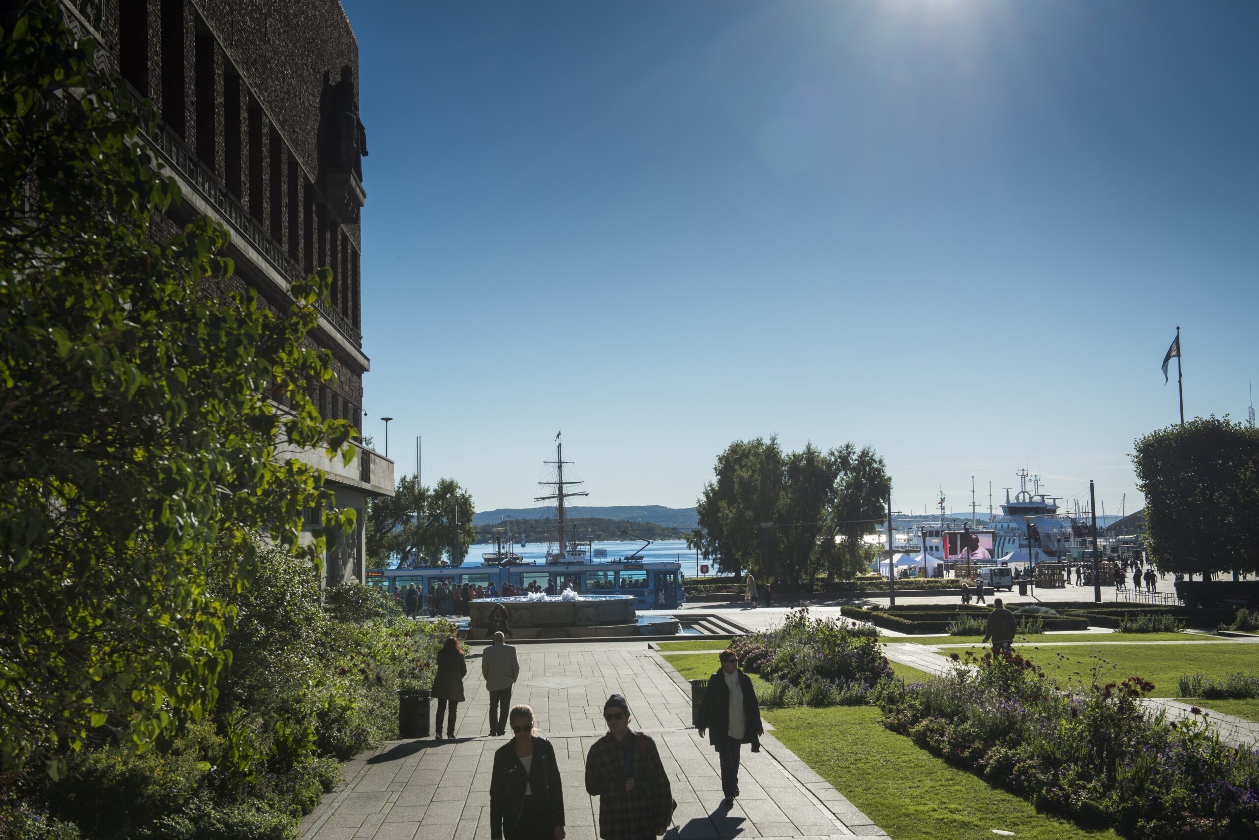 Mennesker gående i solskinn ved Oslo Rådhus.