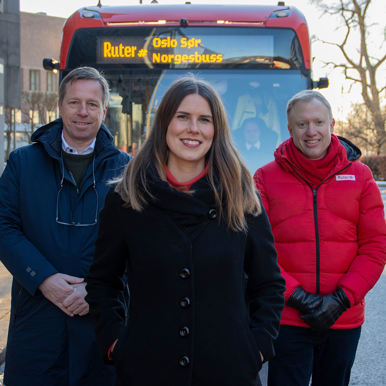 En kvinne og to menn foran en rød Ruter bybuss