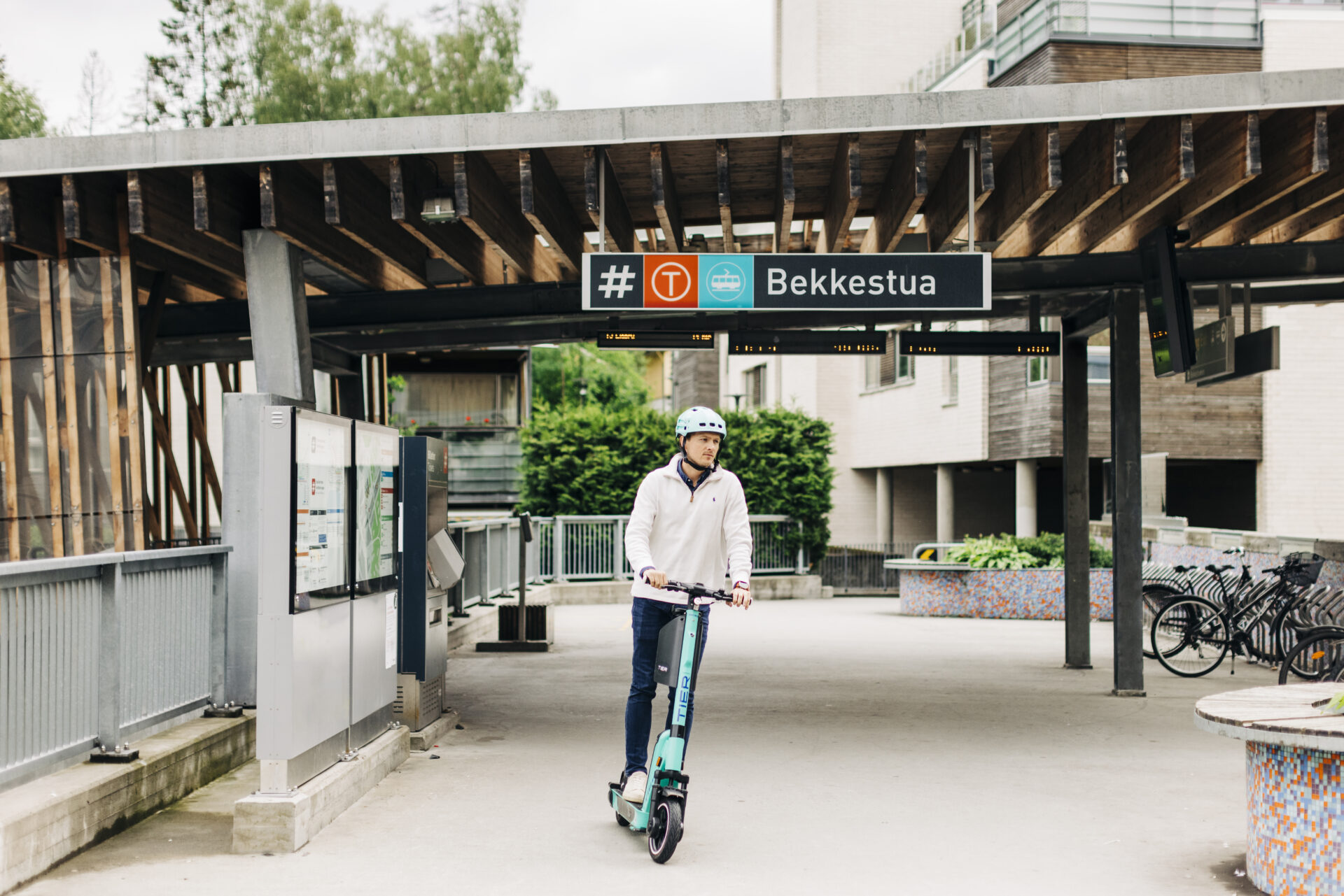 Mann med hjelm på elsparkesykkel på Bekkestua trikk- og t-banestasjon.