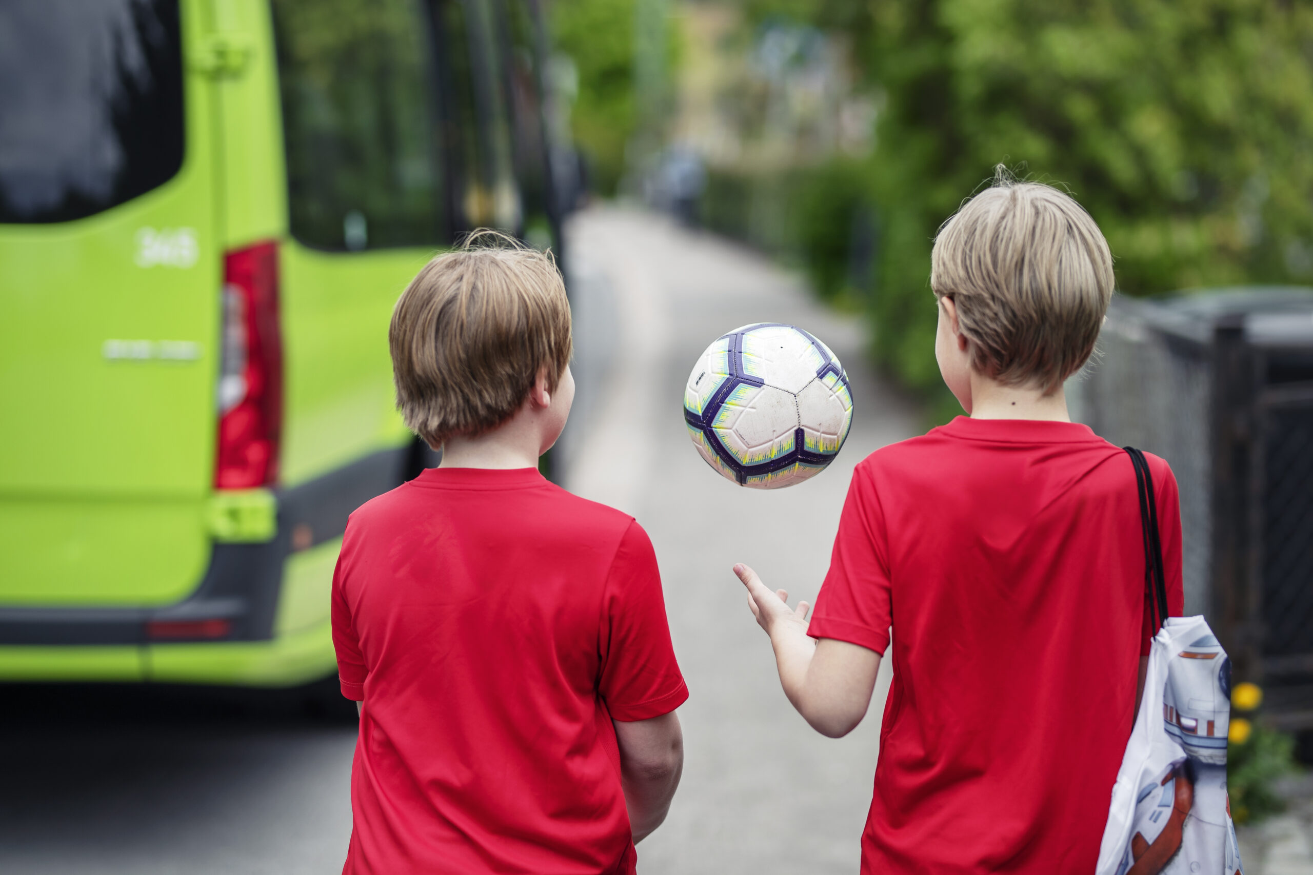 To unge gutter med en fotball gående med en grønn bil for aktivitetstransport i bakgrunnen.