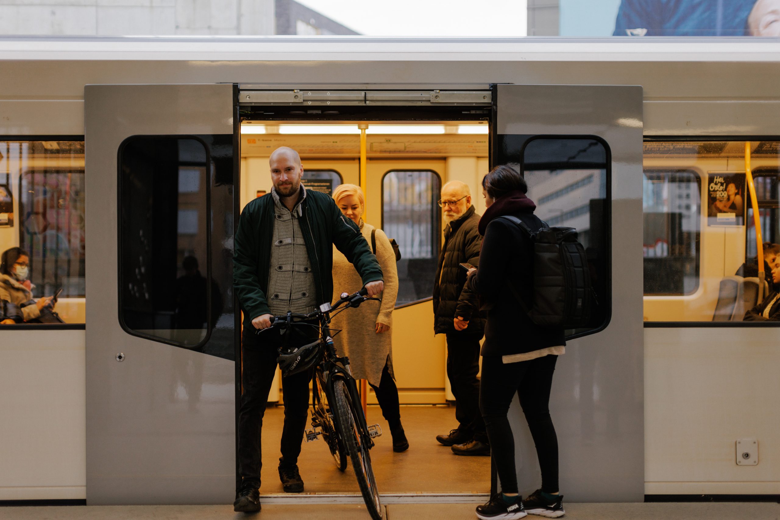 En mann med sykkel stiger av en t-banevogn samtidig som en kvinne med sekk er i ferd med å stige på vognen.