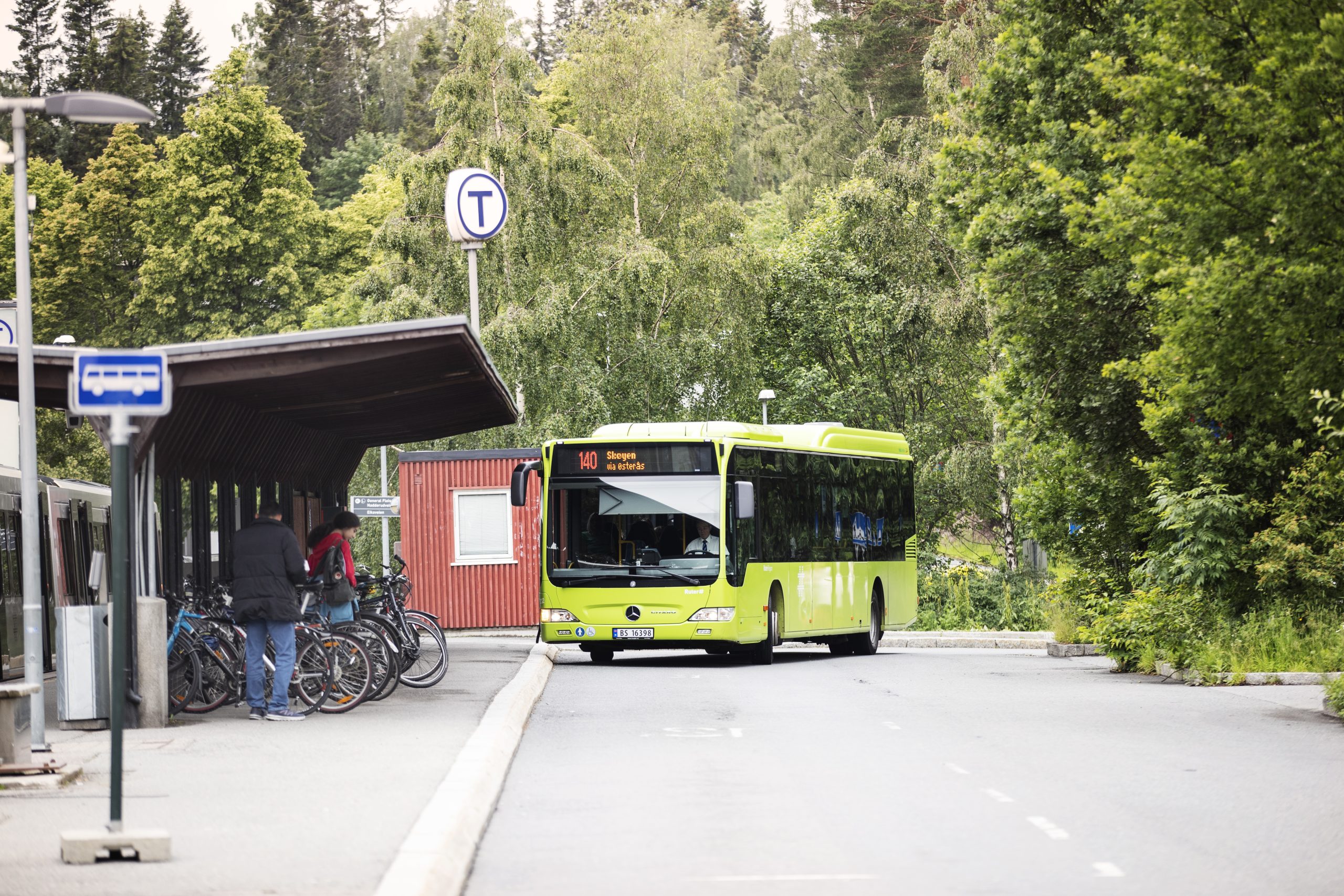 En grønn regionbuss kjører inn på en holdeplass som også inkluderer sykkelparkering og en t-banestasjon.