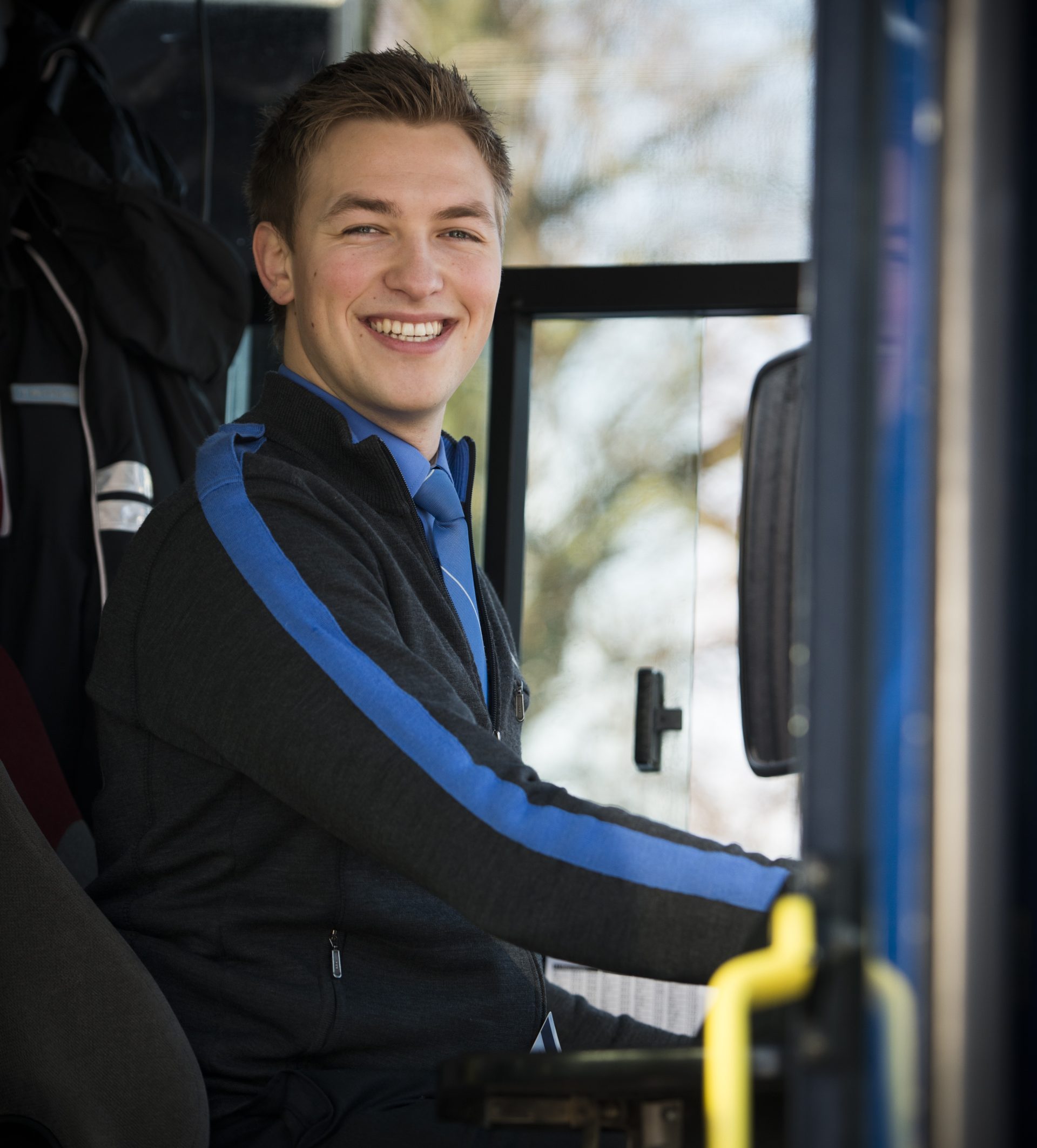 Ung, mannlig bussjåfør ser smilende inn i kameraet.