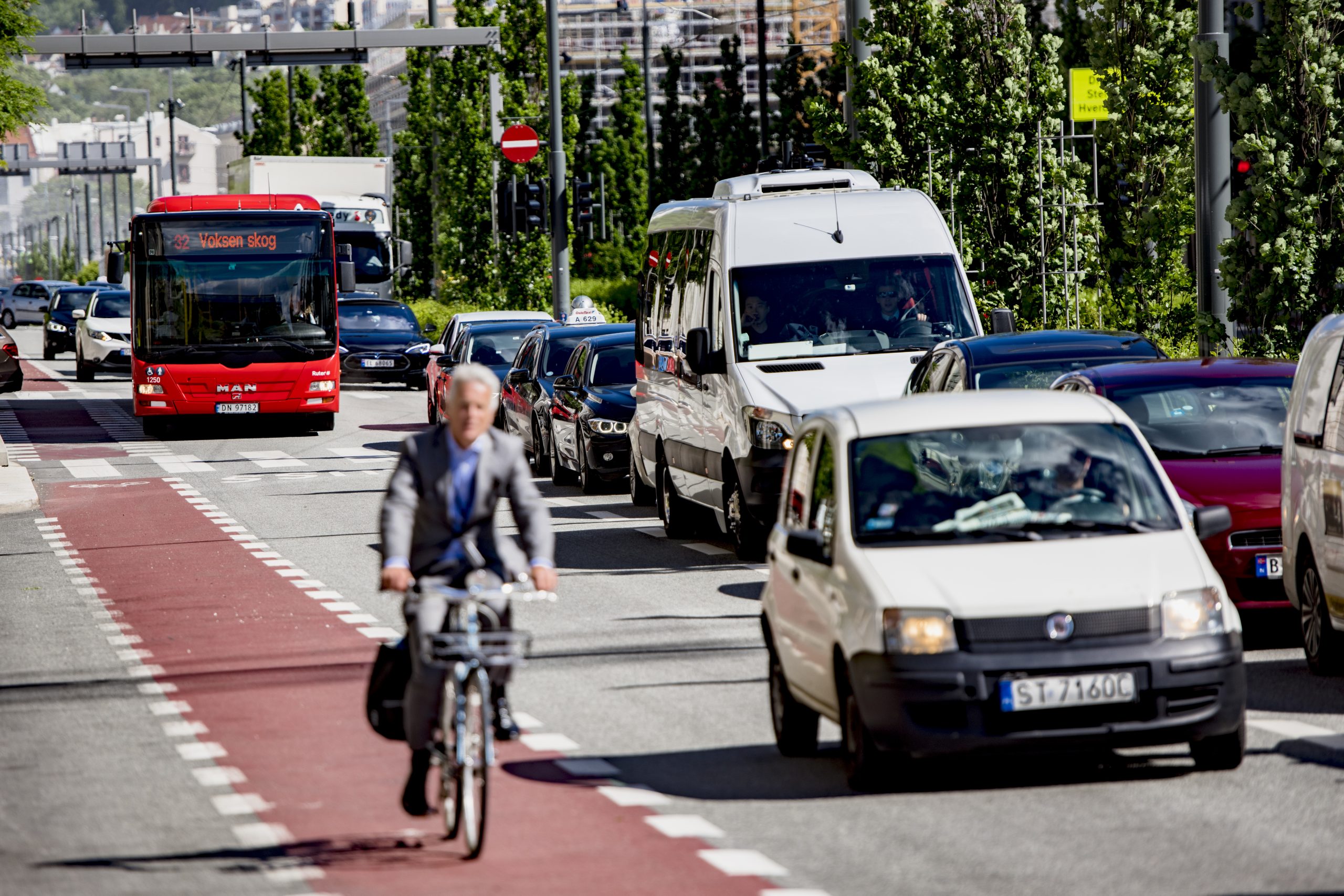 En mann sykler på sykkelsti ved siden av en traffikert vei.