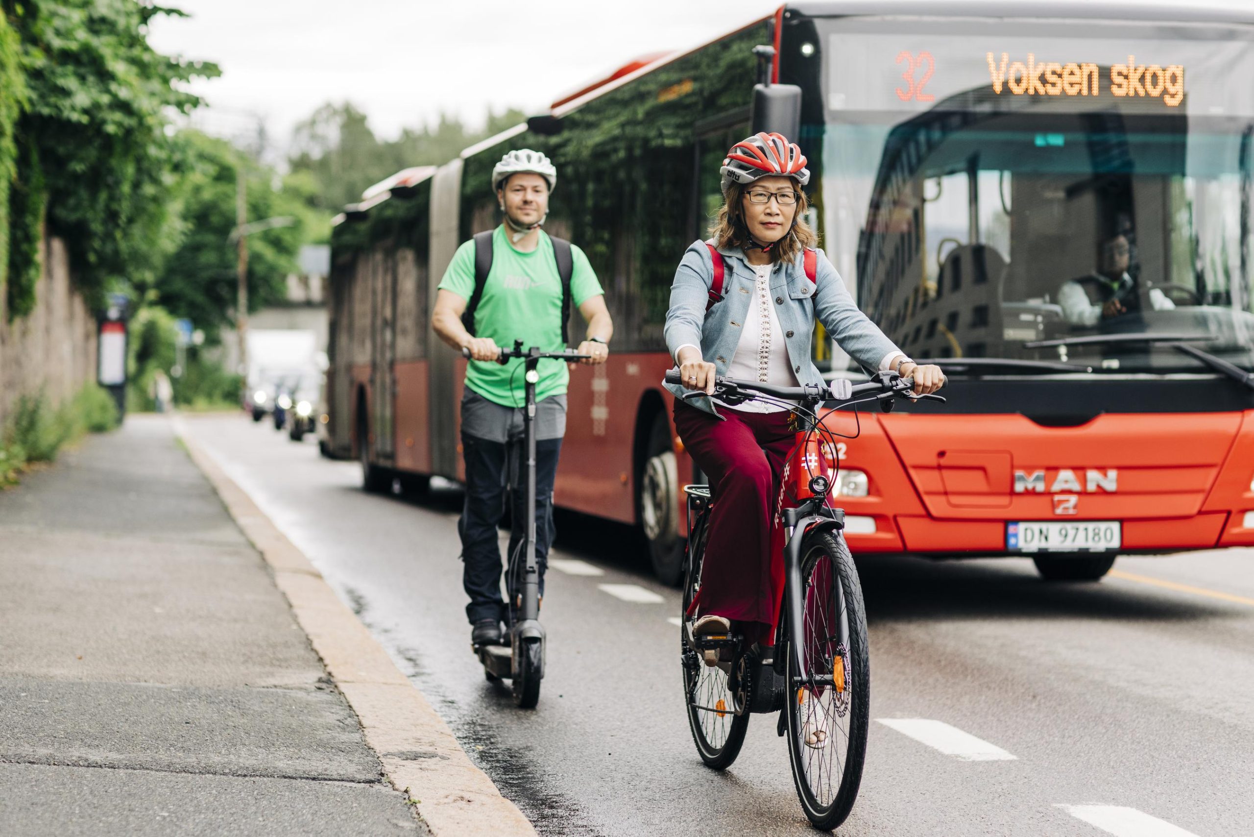 En kvinne på sykkel og en mann på sparkesykkel, i sykkelfelt, kjører forbi en Ruter bybuss.