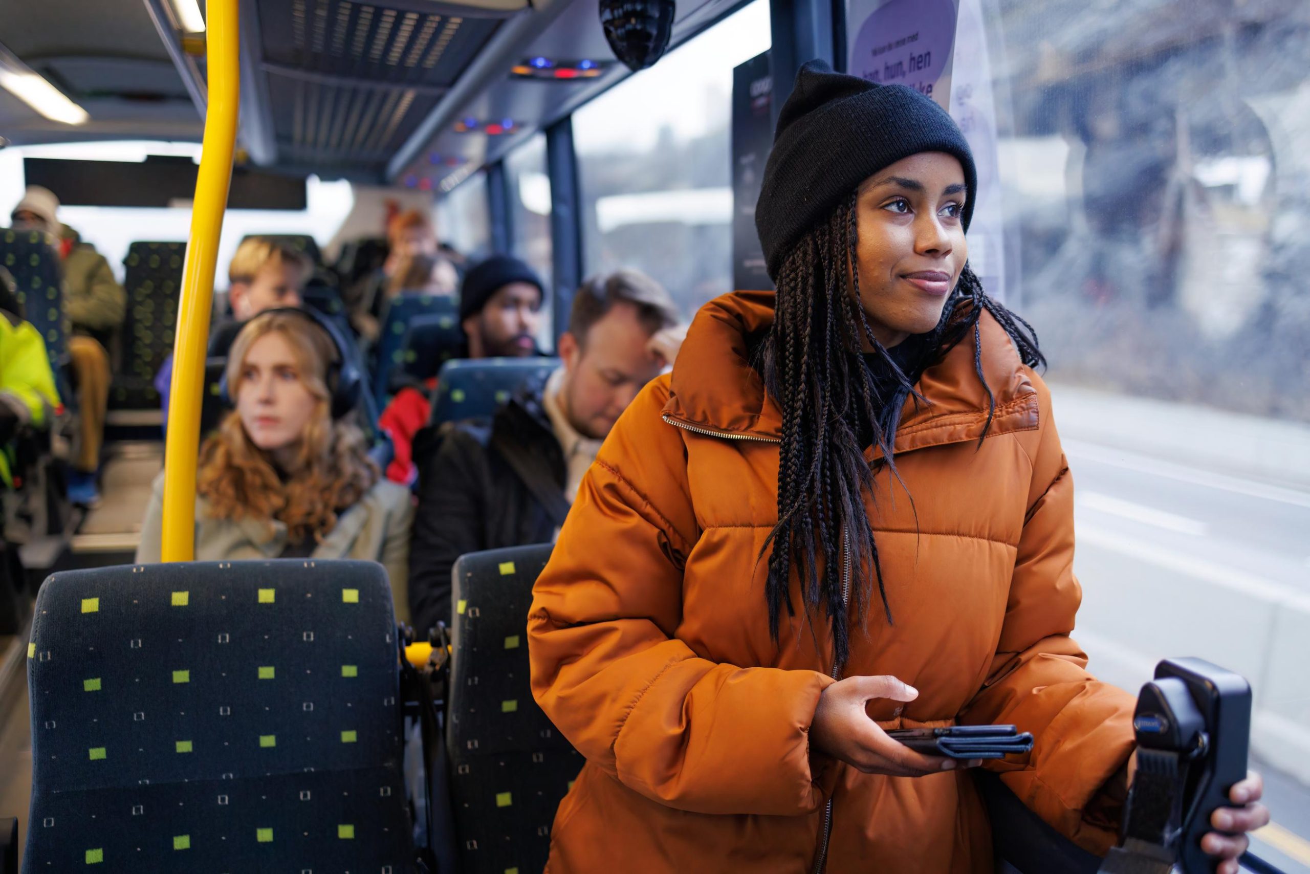 Kvinne stående på en buss ser ut av vinduet, med en mobiltelefon i hånden.