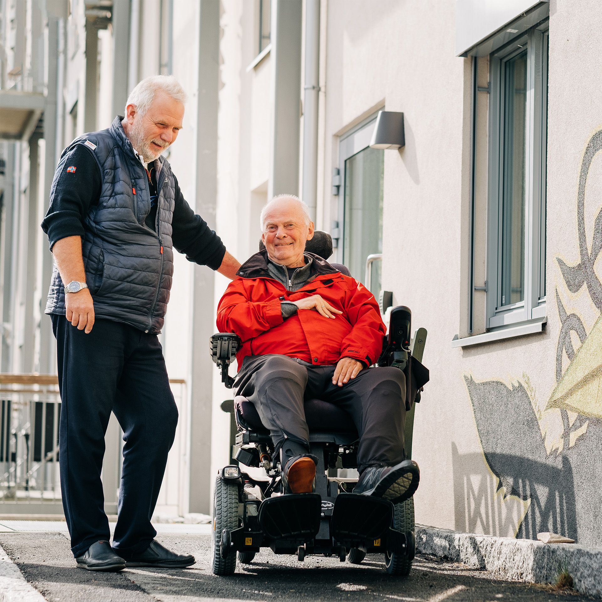 Sjåfør for tilrettelagt transport hjelper en eldre rullestolbruker.