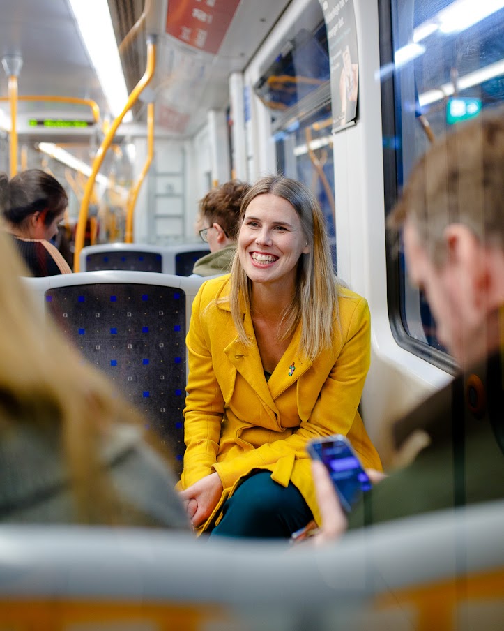 Sirin Stav sits on a subway seat and smiles at a fellow passenger.