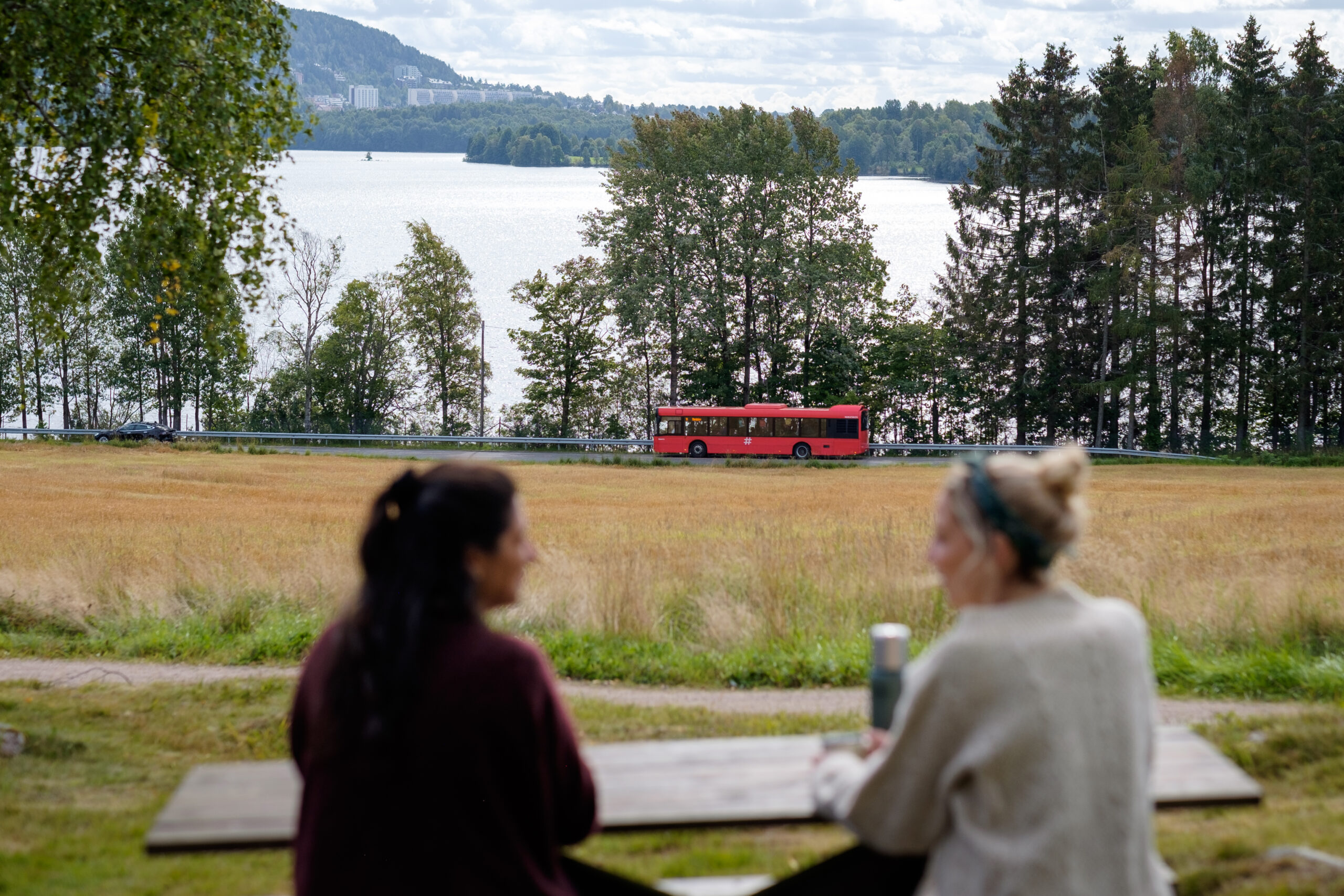 Red bus runs in Maridalen, with two tour girls in the foreground.