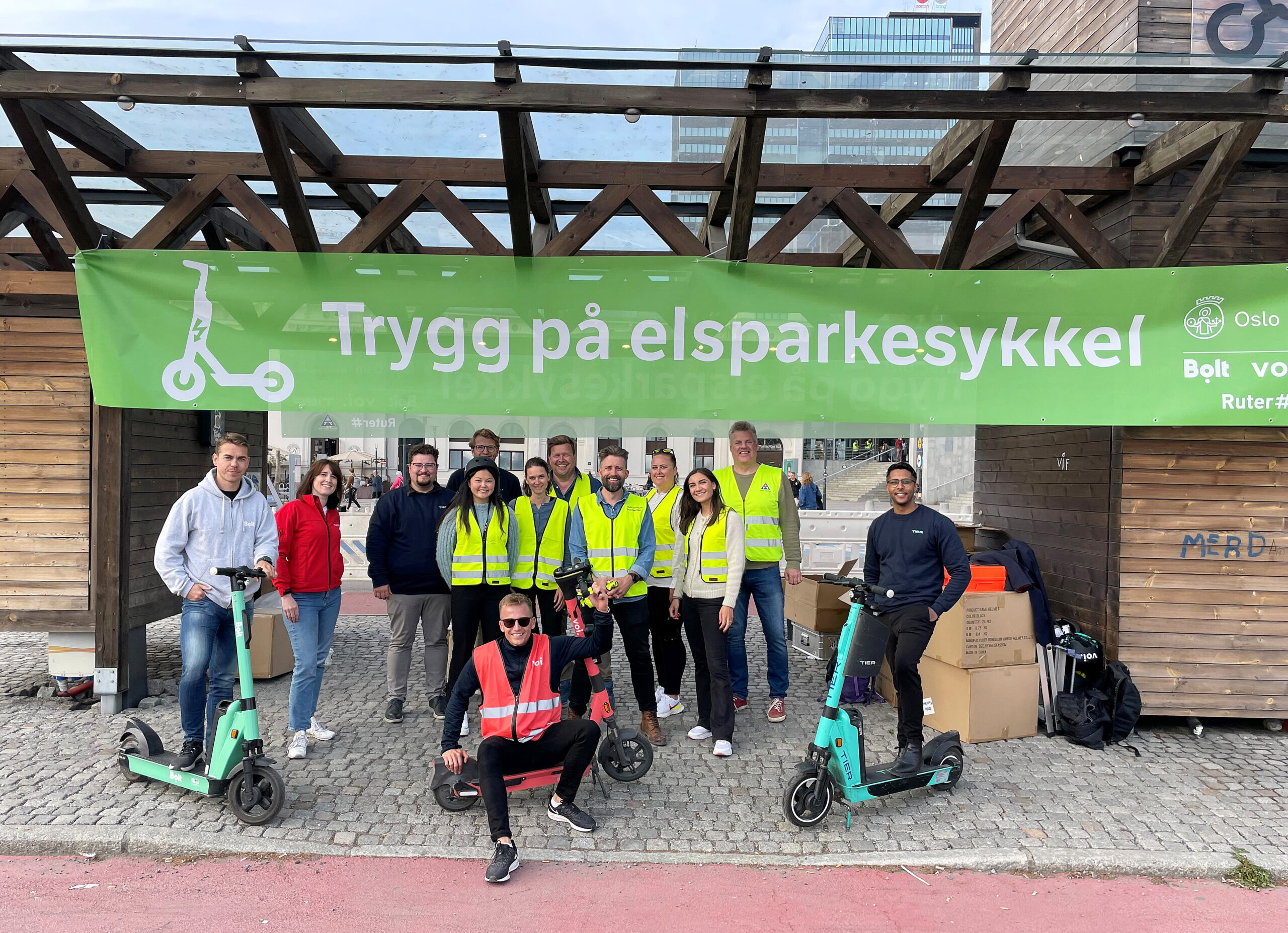 Many people with electric scooters gathered under a green banner with the text "Safe on electric scooters"