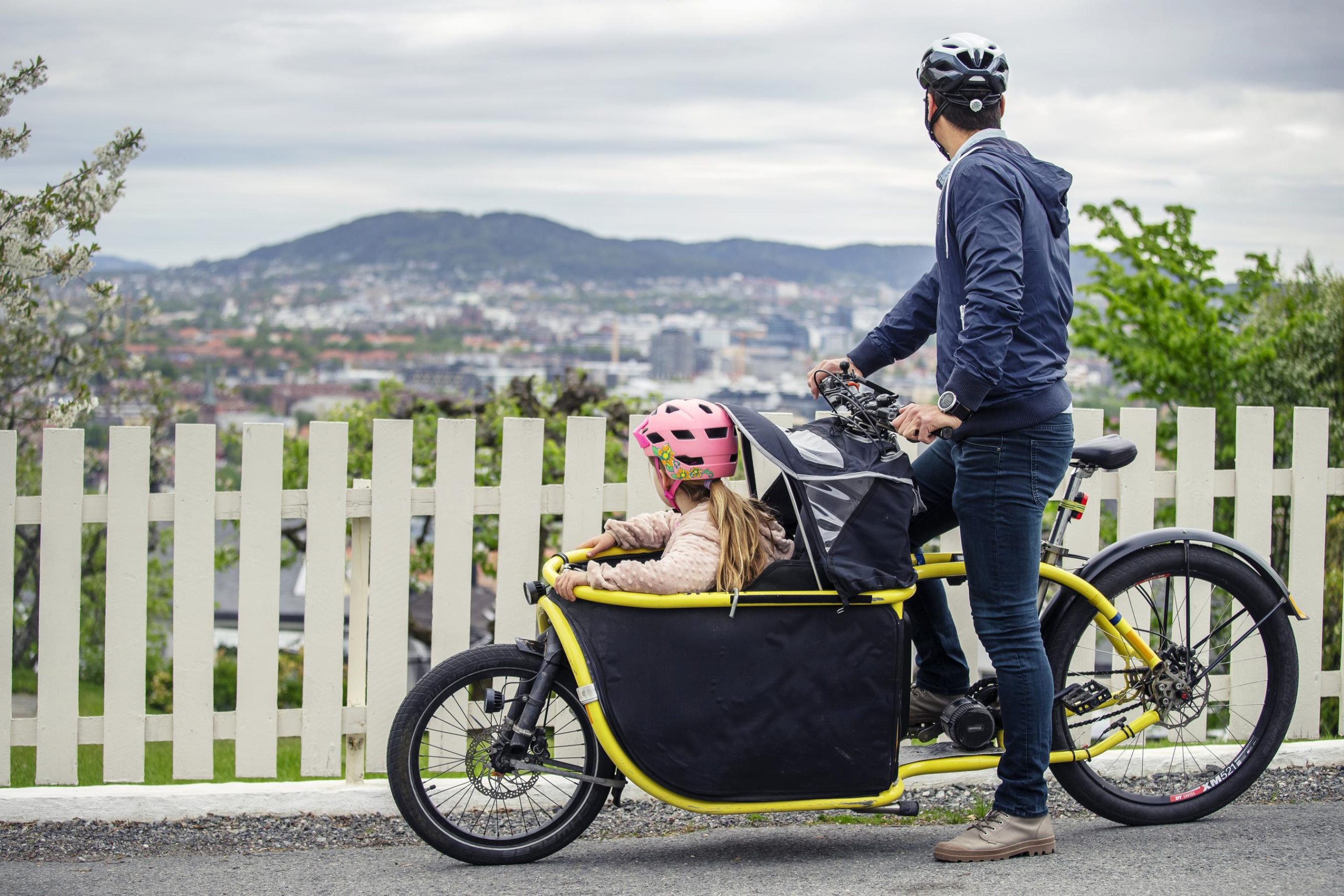 A man and a child on a bike stand still on a hill and view the landscape of Oslo.