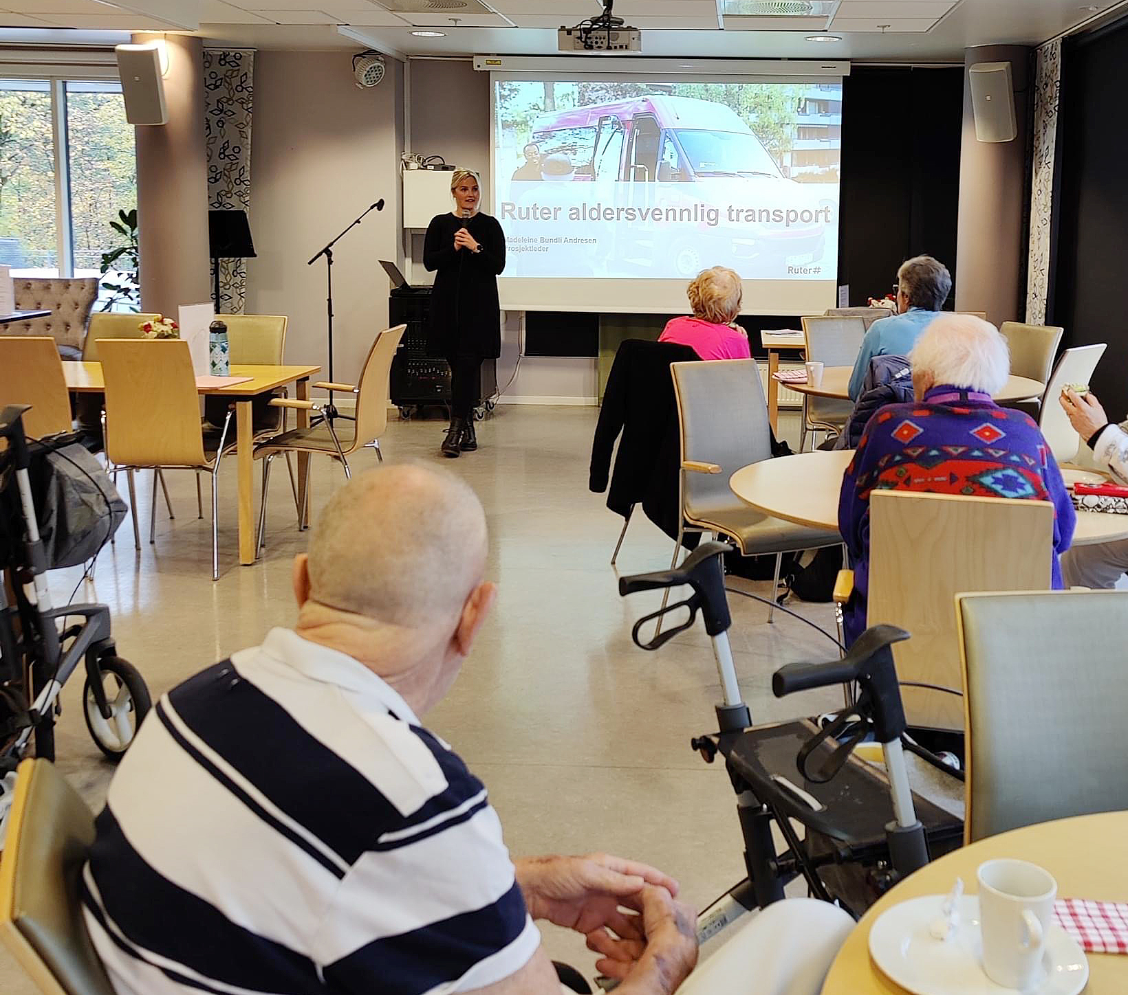 Elderly people listen to a woman present Ruter's age-friendly transport.