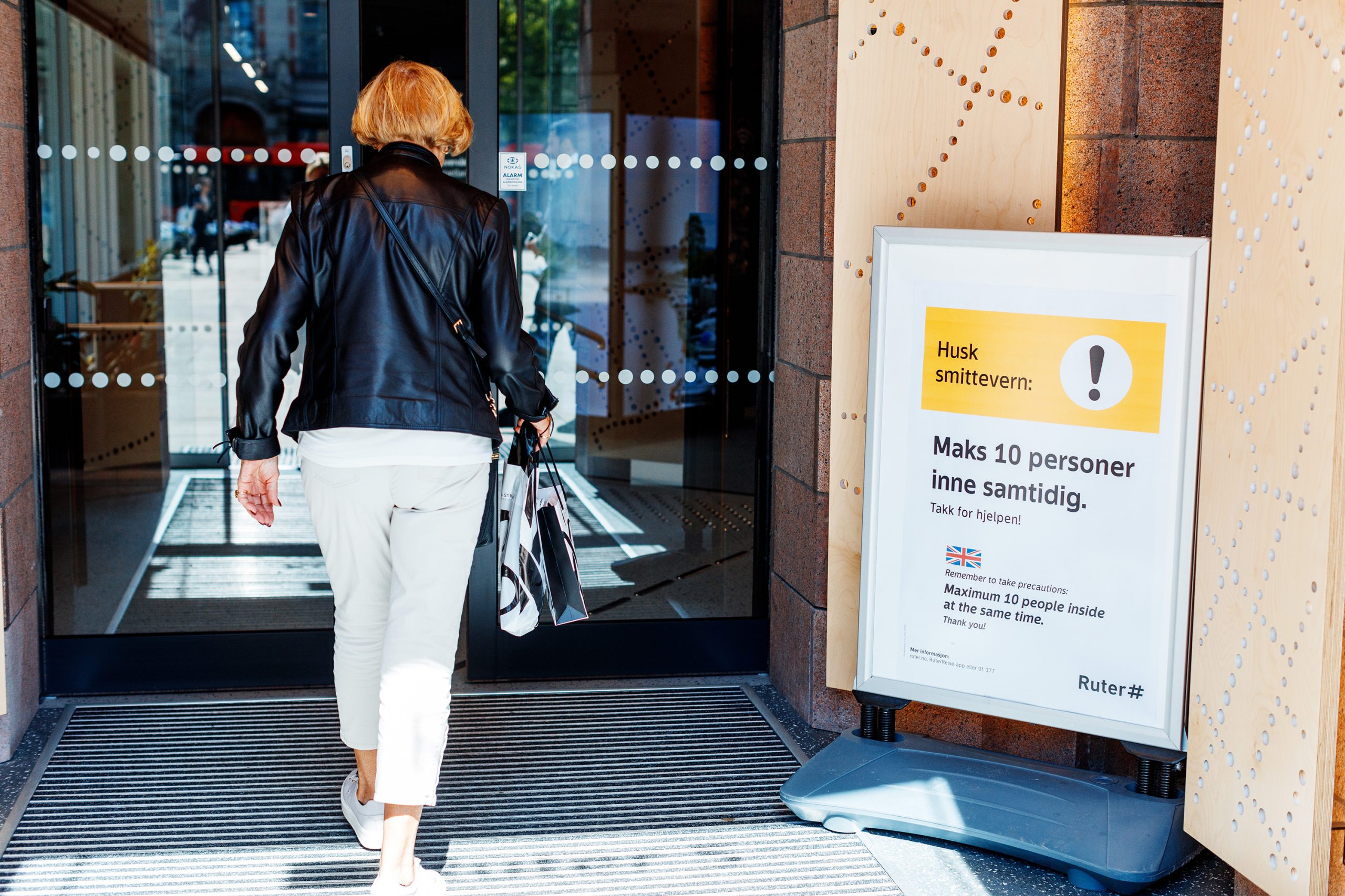 Woman entering a door with an infection prevention poster placed next to the door.